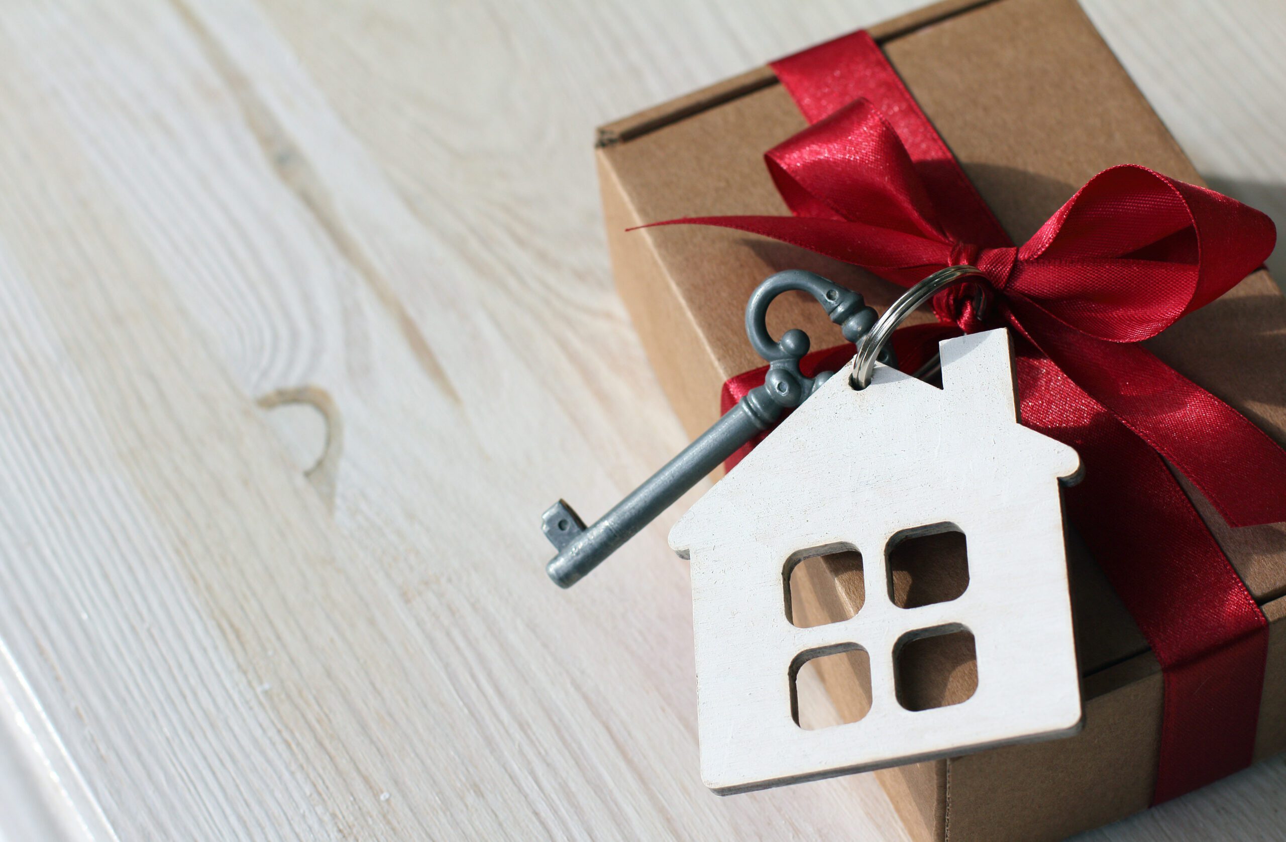 Brown box tied with a key on a house-shaped keychain in a satin red ribbon and bow.