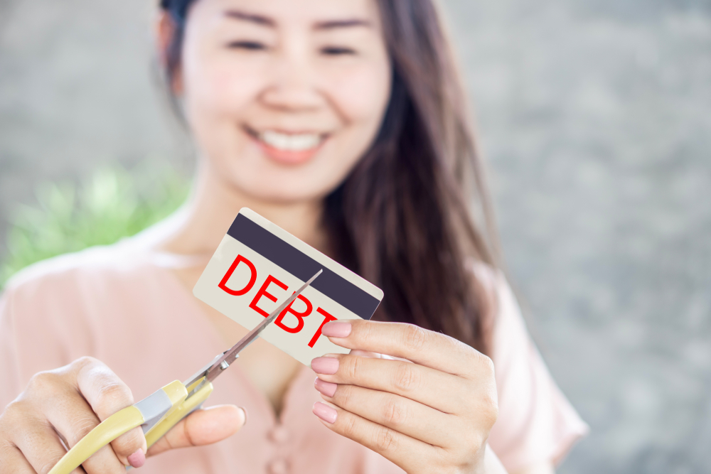 Young woman cutting up a credit card marked "debt."